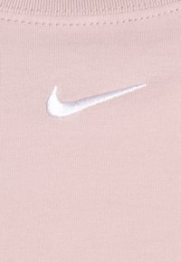 Ljust rosa tyg med en framträdande vit broderad Nike swoosh-logotyp, med en mjuk, slät textur och en åtsittande design.