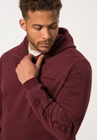 Felpa bordeaux realizzata in morbido tessuto, con cappuccio regolabile, maniche lunghe e un logo discreto sul petto e sulla manica.