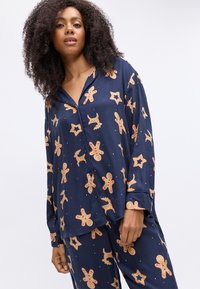 Marineblauw pyjama set met patronen van peperkoeken mannen, sterren en rendieren. Zachte stof, losse pasvorm, knoopshirt met lange mouwen.
