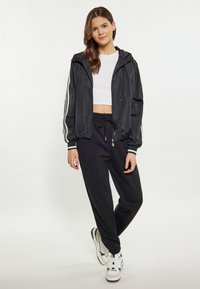 Sort letvægts bomberjakke med hvide striber, parret med sorte joggers. Modellen bærer en hvid crop top og hvide sneakers.