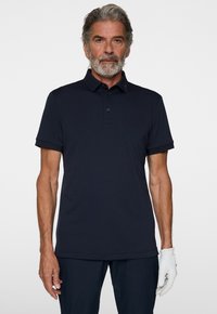 Granatowa koszulka polo z zapięciem na guziki, krótkimi rękawami i subtelnym logo na kołnierzyku. Gładka tekstura i nowoczesny krój.