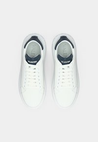 Ζευγάρι λευκά αθλητικά παπούτσια Valentino με μαύρες ταμπέλες στα τακούνια και κορδόνια, από πάνω σε απλό ανοιχτό φόντο.