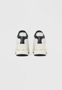 Bele in mornarsko modre superge z obliko na podplatu, ki vključujejo materiale iz semiša in usnja, teksturirane poudarke ter zaobljen zadnji profil.