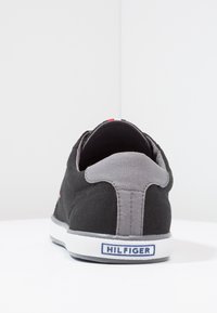 Sneaker in tela nera con pannello posteriore grigio e suola in gomma bianca. Presenta il logo del marchio in blu sul tallone e accenti di colore sottili sulla parte superiore.