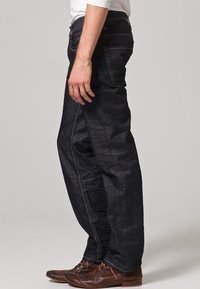 Mörkblå jeans i denim med rak passform, synliga sömmar och en lätt textur; kombinerade med bruna läderskor.