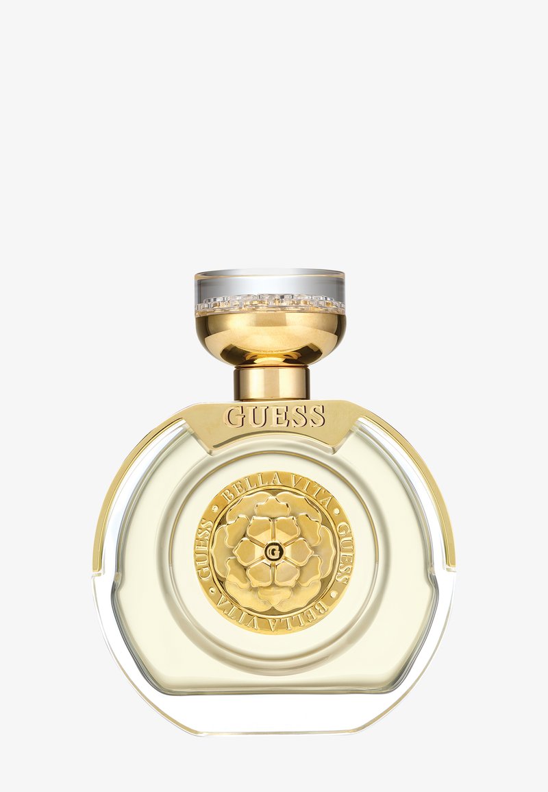 Runde, klare Parfümflasche mit goldenem Rand, einem goldenen Blumenemblem mit der Aufschrift "Guess Bella Vita" und einem goldenen sowie transparenten Deckel.