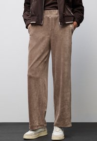 Hnědé kordové kalhoty se hladkým povrchem, širokými nohavicemi a bočními kapsami, kombinované s bílými teniskami.