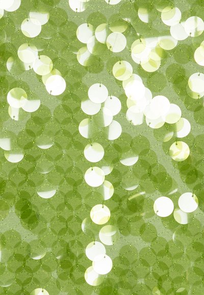 Zöld szövet, melyet különböző árnyalatú, kör alakú flitterek díszítenek, texturált, fényvisszaverő felületet alkotva, ahol a fény a fényes lemezeken játszik.