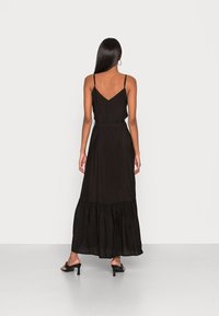 Černé maxi šaty s tenkými ramínky, rozšířeným lem a vrstvenými volány. Vyrobeno z lehké tkaniny s hladkou strukturou.