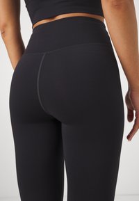 Mustat korkeavyötäröiset legginsit, jotka on valmistettu joustavasta kankaasta. Ne ovat sileätekstuuriset ja niissä on huomaamaton saumaus takana.