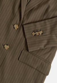 Brązowa marynarka w prążki z guzikami w kolorze żółwia z przodu oraz trzema guzikami przy mankietach.