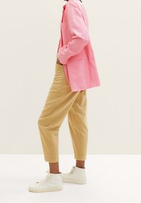 Svetle růžový blazer s dlouhými rukávy, přes béžové zkrácené kalhoty, doplněný bílými vysokými teniskami. Blazer má uvolněný střih a boční kapsu.