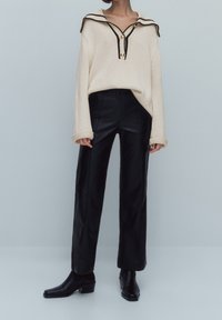 Pull en tricot beige avec un grand col et des finitions noires, associé à un pantalon en cuir noir taille haute et des bottines noires.