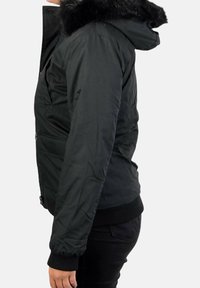 Sort dunjakke med pelsforet hætte, der har elastiske manchetter, frontlommer og lynlås, med en glat, mat tekstur.