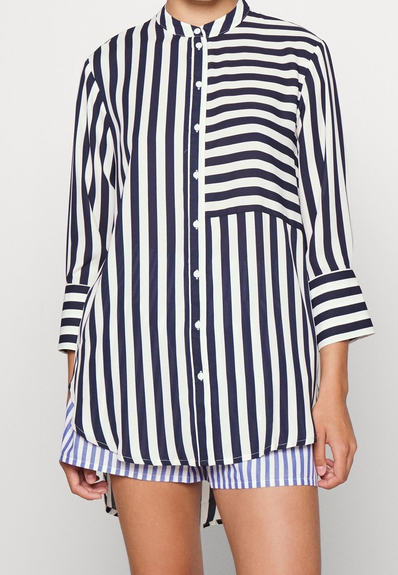 Camicia a righe blu navy e bianco con colletto alla coreana, maniche a tre quarti e tasca frontale; tessuto morbido con vestibilità ampia.