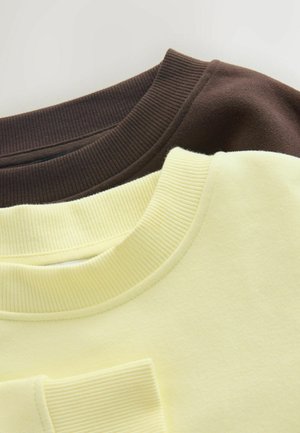 Hnědé a žluté mikiny naskládané na sobě, s žebrovanými límečky. Hnědá mikina má jemnou texturu, zatímco žlutá je hladká a mírně tlumená.