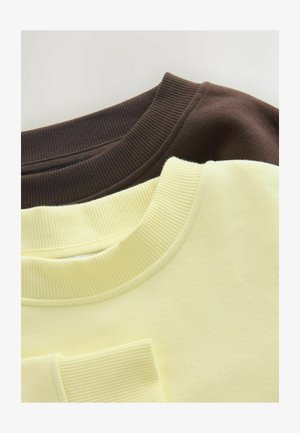 Hnědé a žluté mikiny naskládané na sobě, s žebrovanými límečky. Hnědá mikina má jemnou texturu, zatímco žlutá je hladká a mírně tlumená.