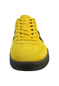 Gelbe Wildleder-Sneaker mit schwarzen Akzenten, runder Zehenpartie, flachen Schnürsenkeln und Gummisohle. Eckige Nähte sind über das gesamte Schuhwerk verteilt.