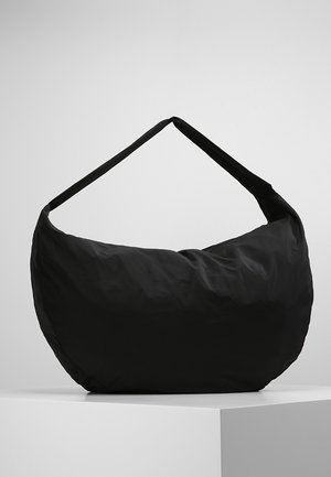 Black soft fabric shoulder bag with wide strap, displayed on white pedestal against plain light background.