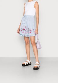 Jasnoniebieska plisowana spódnica z haftowanymi kwiatami u dołu, zestawiona z białym topem bez rękawów, białymi sandałami i małą lawendową torebką.