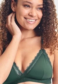 Soutien-gorge triangle vert avec dentelle, fabriqué en tissu doux, doté de bretelles ajustables et d'une bande texturée avec détail de marque.