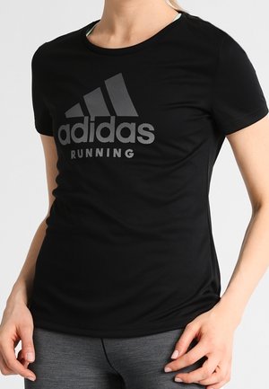 Persoon draagt een zwart Adidas Running T-shirt en grijze sportlegging, zichtbaar van nek tot heupen met handen rustend nabij de heupen.