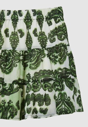Stufenrock mit grünen und dunkelgrünen Paisley-Mustern auf weißem Faltenstoff.