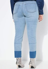 Hellblaue Jeans aus Denim mit einem farblich abgesetzten Saum, der zwei Blautöne beinhaltet. Rückentaschen und ein Slim-Fit-Design.