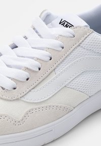 White sneaker with mesh and suede panels, featuring a white leather side stripe and white laces. Textured accents and rubber sole.