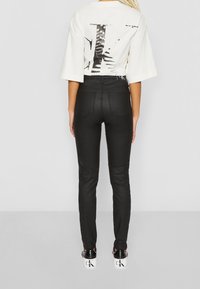 Czarne dżinsy o dopasowanym kroju z tylnymi kieszeniami, w zestawie z białym oversize'owym t-shirtem z dużą czarną grafiką na plecach.