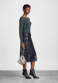 Λαμπερή πράσινη μπλούζα με μακριά μανίκια, σε συνδυασμό με φούστα σε ναυτικό μπλε διακοσμημένη με παγιέτες. Μαύρες μποτάκια έως τον αστράγαλο με χρυσές λεπτομέρειες και ασημένια τσάντα.