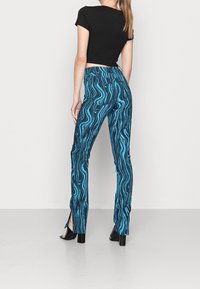 Blå mönstrade byxor med en vågig design, tillverkade av en blandning av material. Har sidoflikar vid fållen och en hög midja.