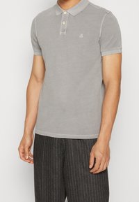 Ljusgrå polo skjorta med klassisk krage, två knappar och en liten logotyp på bröstet. Kortärmad med en mjuk textur.