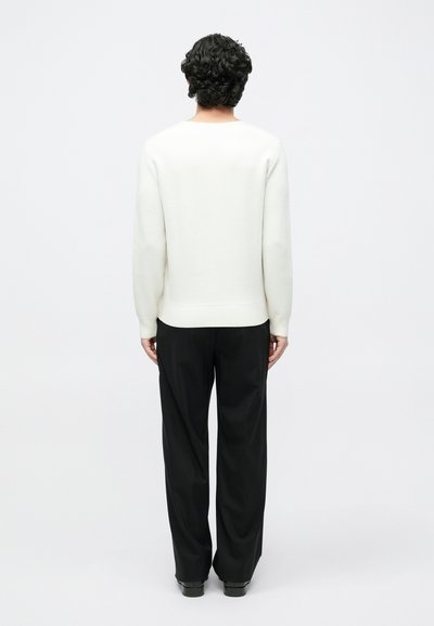 Λευκό πλεκτό πουλόβερ με στρογγυλή λαιμόκοψη και ριμπ τελείωμα, συνδυασμένο με μαύρο παντελόνι, σε εικόνα από πίσω. Ομαλή υφή και άνετη εφαρμογή.
