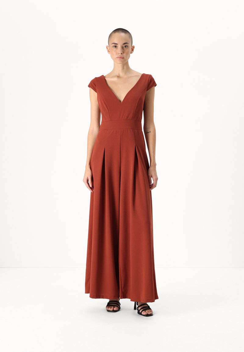 Jumpsuit boje rđe s dubokim V-izrezom, kratkim rukavima i plitkim širokim nogavicama. Glatka, mekana tkanina elegantno pada.