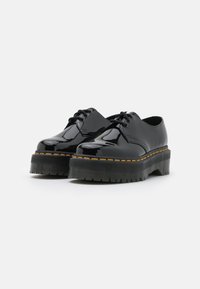 Scarpe in pelle verniciata nera con suola spessa, caratterizzate da cuciture arancioni lungo il bordo e lacci neri. Design a punta rotonda e suola testurizzata.