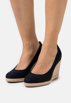 Námořnické modré semišové wedges s mandlovou špičkou, které mají textura z juty kolem platformy pro přidanou výšku a designový prvek.
