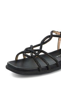 Czarne płaskie sandały z krzyżującymi się paskami wykonanymi z teksturowanego materiału. Posiadają gładką podeszwę i matowe wykończenie, zaprojektowane z myślą o komforcie.