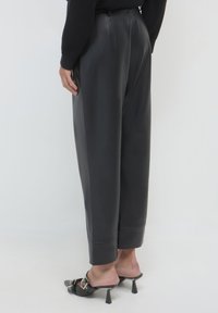Pantaloni in pelle nera con una vestibilità ampia, caratterizzati da un alto punto vita, orlo a risvolto e una texture liscia, abbinati a mule nere con tacco.