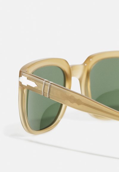 Óculos de sol com uma armação translúcida em bege, lentes verdes e um design elegante. Acento metálico notável na haste.