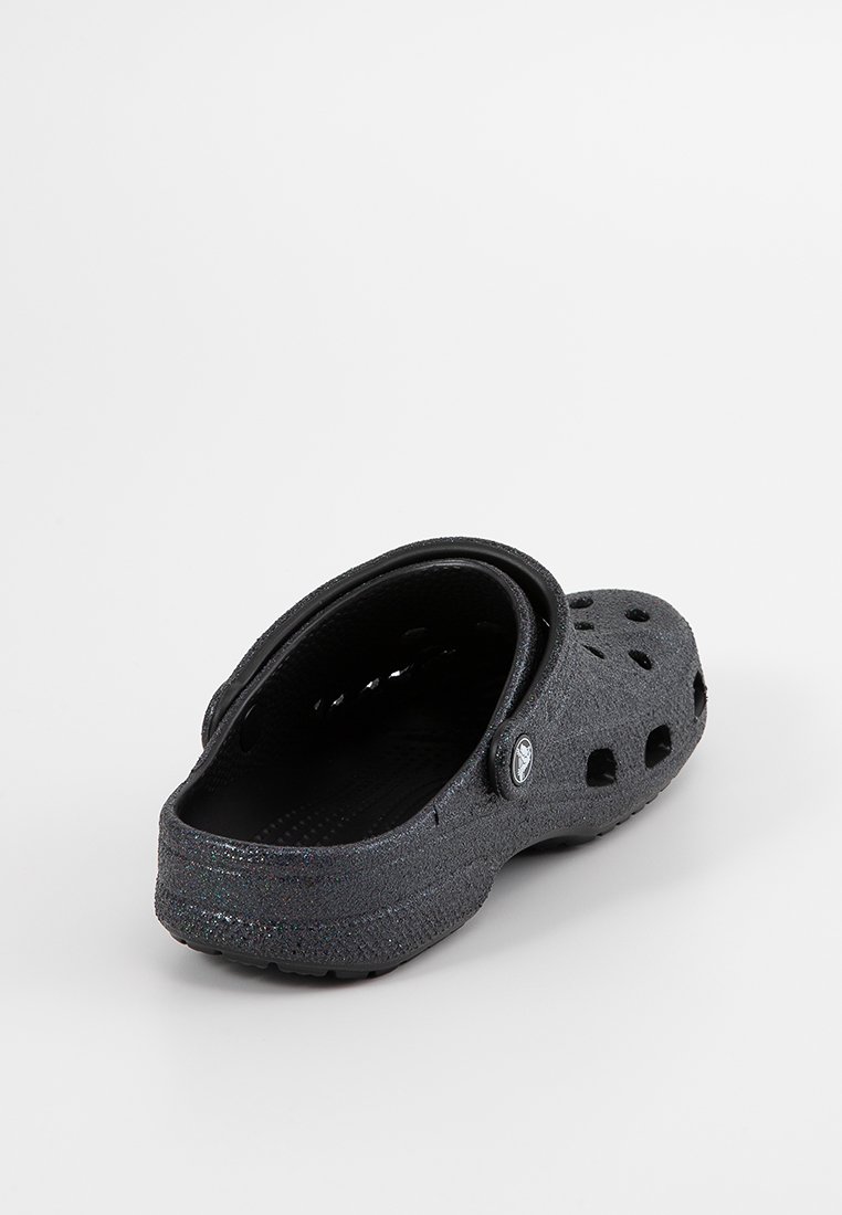 Schwarzer, wasserdichter Clog im Krokodil-Look mit Belüftungsöffnungen, strukturierten Oberflächen und gebogenem Riemen für einen sicheren Sitz; flache Sohle für Komfort.