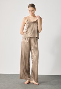 Satin-pyjamasetti vaaleanruskeana, jossa on pystysuorat raidat. Toppi ohuilla olkaimilla ja löysät, leveät housut. Pehmeä pinta.