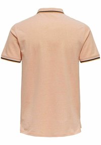 Polo de manga corta en tejido melocotón claro. Presenta un collar con rayas negras y naranjas en los bordes. Textura suave.