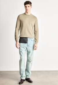 Beżowy sweter z dzianiny z okrągłym dekoltem, zestawiony z jasnoniebieskimi dżinsami o prostych nogawkach. Charakterystyczna czarna skórzana saszetka noszona na talii oraz brązowe buty.