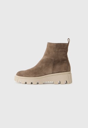 Brown suede ankle boots with a chunky beige sole and jagged edges, featuring a pull tab at the back for easy wear.
