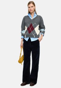 Szary sweter warkoczowy w romby w kolorze bordowym i kremowym, nałożony na jasnoniebieską koszulę. W połączeniu z ciemnymi, szerokimi spodniami z corduroy i żółtą torebk�ą.