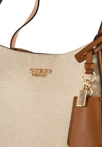 Beige strukturierte Tragetasche mit glattem braunem Lederakzent. Verfügt über goldene Hardware und einen markierten Schlüsselanhänger. Verstellbarer Schulterriemen.