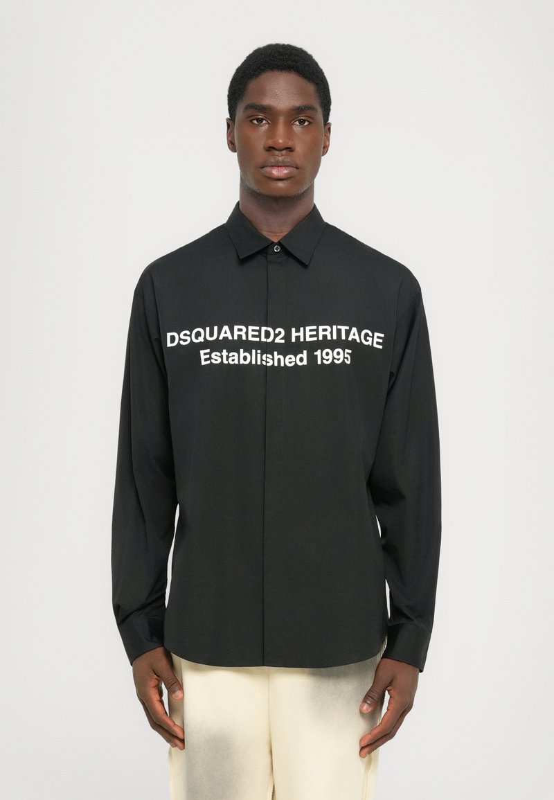 Musta pikkade varrukatega särk, millel on valge kiri: "DSQUARED2 HERITAGE Asutatud 1995." Nuppudega disain klassikalise kraega. Sile tekstuur.
