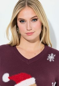 Suéter de punto morado con escote en V, que presenta un diseño de Santa y detalles de copos de nieve en blanco. Textura suave y decoración temática navideña.