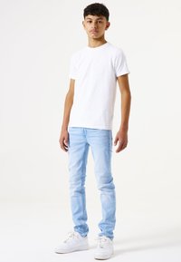 Camiseta de algodón blanca, jeans slim-fit de color azul claro, zapatillas blancas. Conjunto informal con un diseño simple y una paleta de colores minimalista.